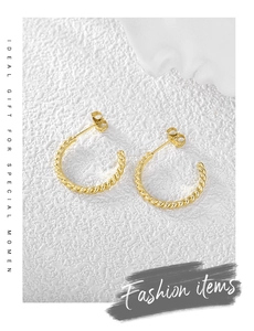 Detail of gold-plated spiral twist earrings on a textured white surface with fashion text