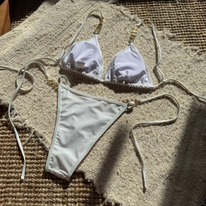 Detail of white bikini with gold metal chain accents and size S tag on textured mat