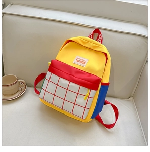 Detail of color-block canvas kids backpack with BE YOURSELF label on smooth sofa