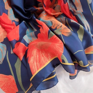 Detail of silk scarf with red flower print on blue fabric over white carpet