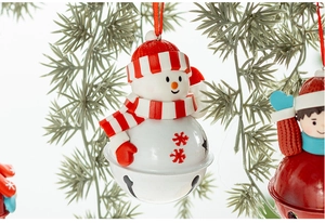 Detail of a snowman Christmas bell ornament with red snowflakes on a pine branch background