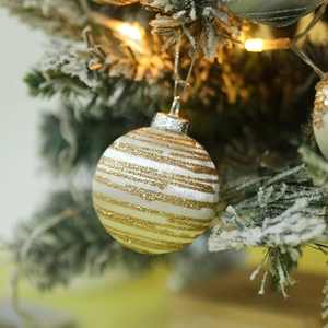 Macro shot of a white Christmas ball with gold stripes hanging on a snowy pine branch