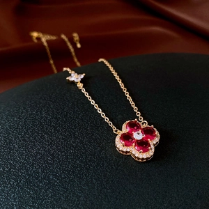 Detailed macro view of gold clover pendant with red gemstones and sparkling zircon accents