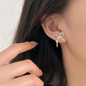 Close-up of a silver bow earring with a pearl drop on model's ear, elegant and dainty style