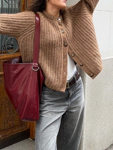 Close-up of brown chunky knit buttoned cardigan with a large red tote bag in a street look