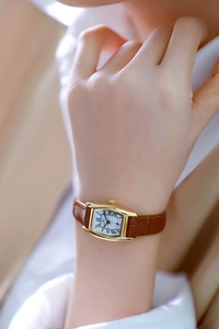 Detail of elegant rectangular gold watch with brown leather strap worn on wrist