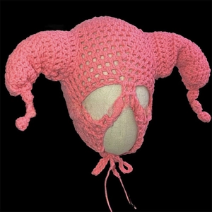 Detail of pink hand-knitted hat with devil horns and earflaps in thick yarn texture