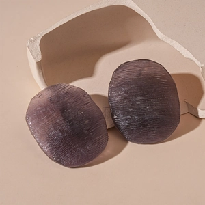 Detail of dark purple acrylic stud earring with horizontal brushed texture on beige stand