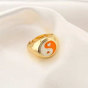 Detail eines vergoldeten Yin-Yang-Herzrings mit orange-weißem Emaille auf Seidenstoff