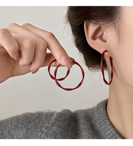 Close-up of deep red twisted wavy hoop earrings worn by a model in a minimalist style