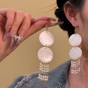 Macro detail of bohemian shell earrings with pearl tassels and gold round accents