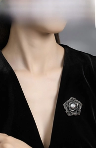 Detailed close-up of a vintage rose brooch with black crystals and a white pearl on a suit