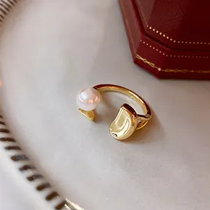 Minimalist gold open ring featuring a white pearl and metallic bead on light background