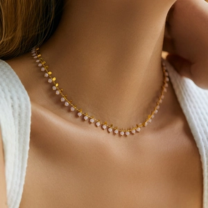 Detail of bohemian necklace featuring small pink beads and golden leaf pendants