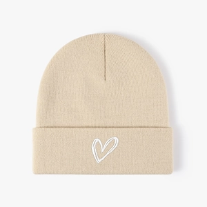 Detail of white heart embroidery on a beige knitted beanie with clear ribbed texture