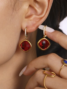 Détail de boucles d'oreilles pendantes en cristal rouge avec placage or et micro-diamants