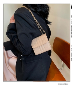 Detail of a beige mini square crossbody bag with gold chain strap worn by a model