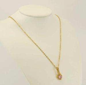 Detailed view of golden necklace featuring a round pink gemstone and white zircon setting