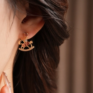 Detail of gold rocking horse earring with red enamel and sparkling zircons on model