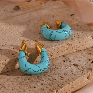 Detailed shot of U-shaped gold earrings with turquoise acrylic marble inlay on stone
