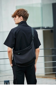 Dettaglio della grande borsa a tracolla in nylon nero con logo verde indossata da uomo