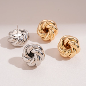 Modern twisted metal knot stud earrings in gold and silver finish on a beige surface