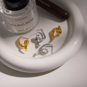 Minimalist 18K gold and silver spiral twist hoop earrings on a white ceramic tray