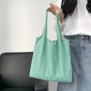 Detail shot of a green and white checkered canvas tote bag held by a model in casual attire