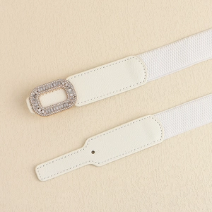 Detail of white elastic waist belt featuring a gold rectangular rhinestone buckle and leather ends