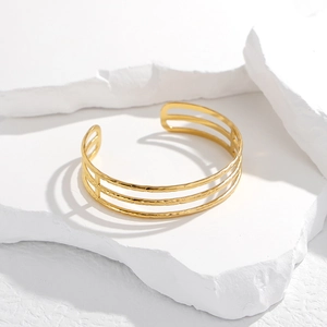 Detail of gold triple-layered open cuff bracelet with hammered texture on white stone