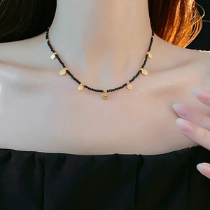 Gros plan d'un collier de perles noires avec petits pendentifs dorés sur un mannequin