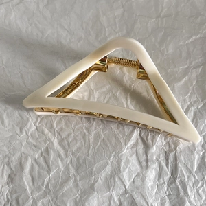 Detail of a French cream triangular hair claw clip with golden metal accents on white paper