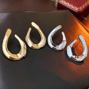 Polished gold and silver twisted U-shaped metal earrings on premium leather background