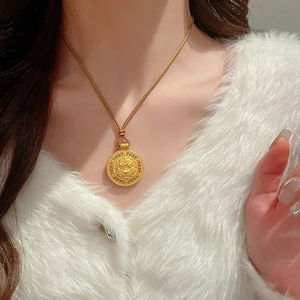 Dettaglio di un ciondolo cilindrico dorato con zircone e rilievo sul collo di una donna