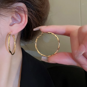 Macro shot of large polished gold-plated hoop earrings with classic pin closure