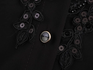 Detailed macro shot of elegant black sequin leaf embroidery and gold-rimmed button