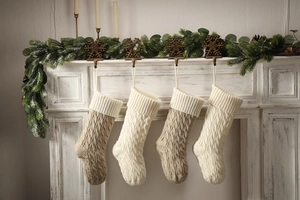 Close-up of four knitted Christmas stockings with cable patterns on a white fireplace