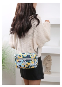 Model shot of a nylon crossbody bag with floral prints and adjustable grey strap