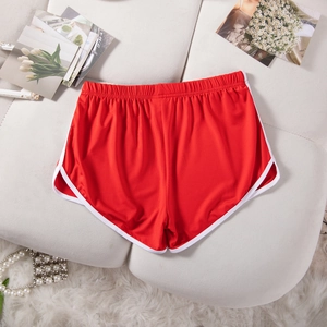 Flat lay view of red athletic shorts with white piping and curved hem on a soft fabric surface