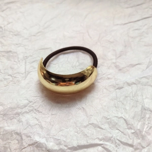 Close-up of a minimalist golden crescent metal buckle on high-elasticity dark brown hair tie