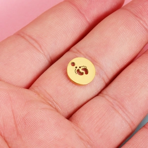 Golden mirror stainless steel round pendant with hollow footprint held in palm for scale