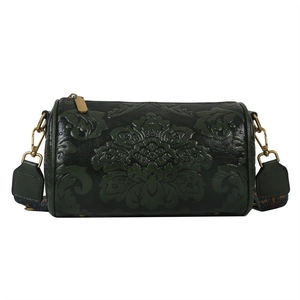 Detailed macro view of retro floral embossed leather on a green cylinder bag with bronze hardware