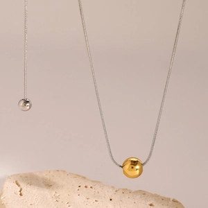 Close-up of minimalist gold and silver bead pendants on snake chain over natural stone