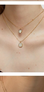 Close-up of double layered gold titanium necklace with white heart and square pendants