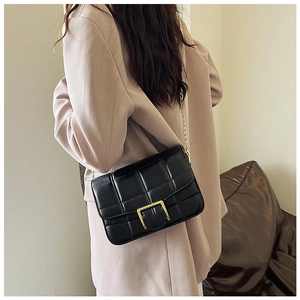 Close-up of black quilted shoulder bag with gold clasp and chain strap on a model