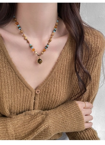 Détail d'un collier de perles vintage avec pendentif rond brun sur un pull col V
