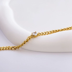 Detailed view of a gold chain bracelet with a single clear round zircon on a white background