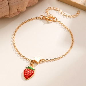 Dettaglio del bracciale dorato con ciondolo a fragola rossa e pendente a cuore