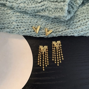Detailed close-up of gold V-shaped stud earrings and cascading tassel chain pendants