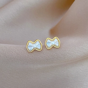 Detail of minimalist bow-shaped earrings with mother-of-pearl texture on silk fabric